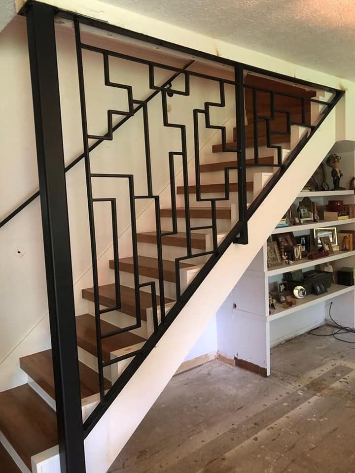 A staircase with wooden treads and a black metal railing featuring a geometric, interlocking square pattern.
