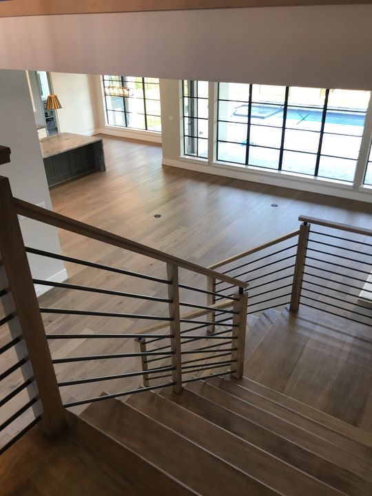 A foyer with light wood floors, beige walls, and a curved staircase featuring black metal railings and wood handrails.