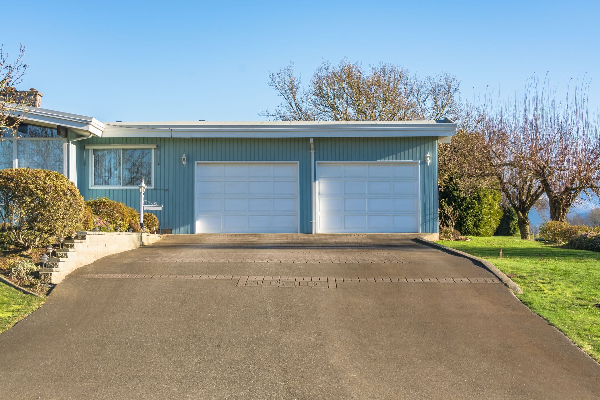 Blue house with two-car garage, gray driveway, and green lawn under a bright blue sky.