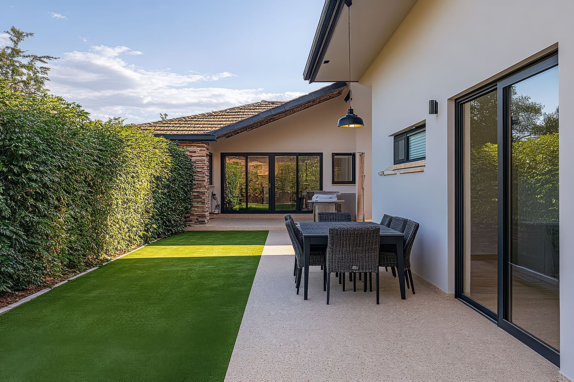 Patio with table and chairs, green lawn, and house with glass doors.