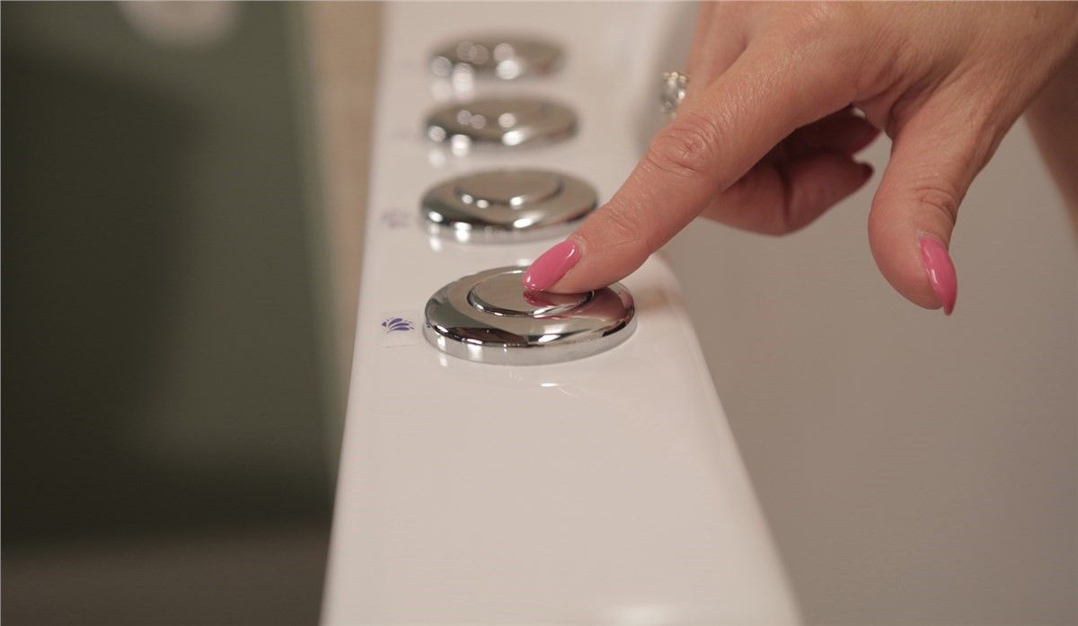 A woman with pink nails is pressing a button on a toilet.