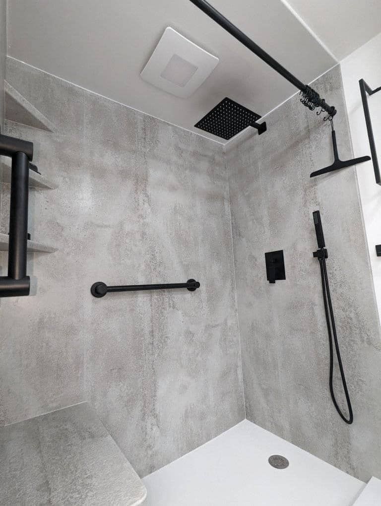A shower with a black shower head and a black railing.