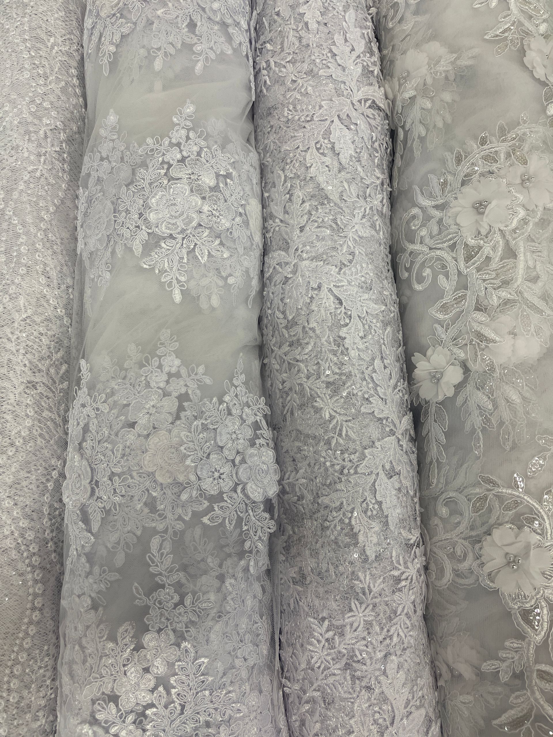 Several rolls of textured, silver-gray lace fabric with floral patterns.