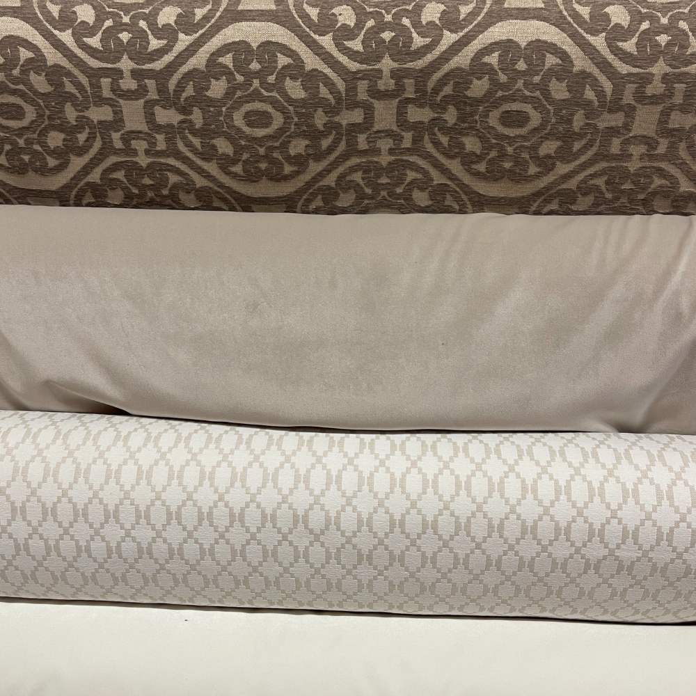 Three rolls of fabric in neutral tones: patterned brown, solid beige, and patterned beige.