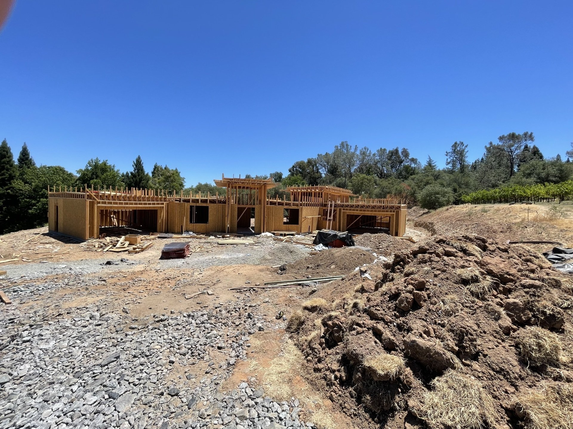 A new house under construction; wooden frame on a dusty, rocky lot under a blue sky. Andrea Lim | Practical Vanity Interiors | Granite Bay, CA | Interior Design