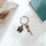 Keys with house charm on a marble surface next to a teal book.