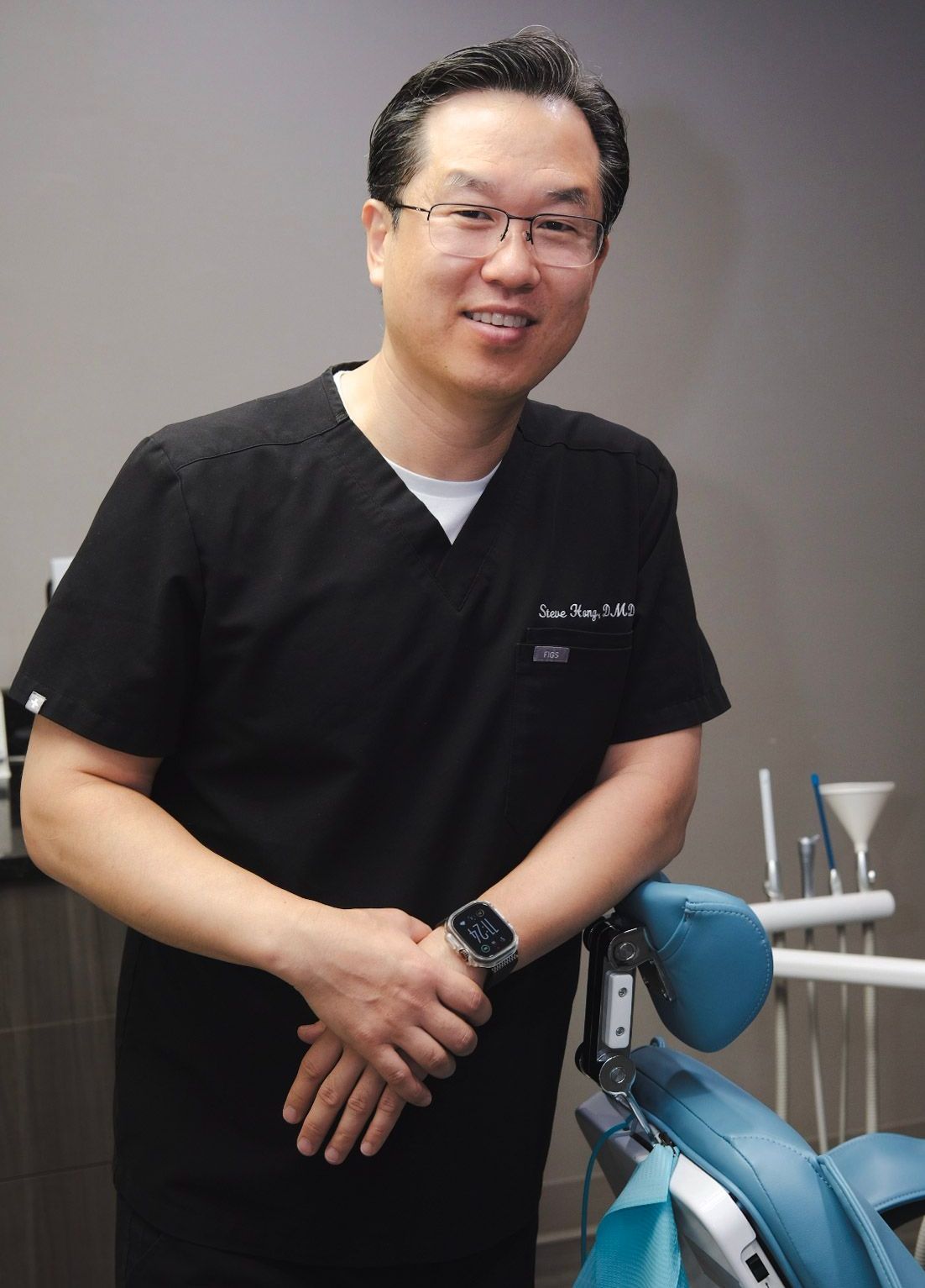 A man in a black scrub is standing in front of a dental chair.