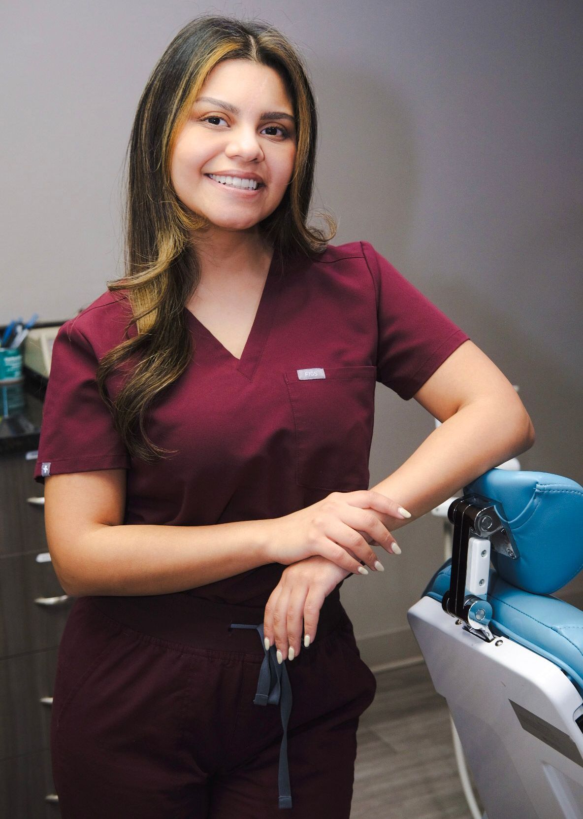 A woman in scrubs is standing in front of a dental chair.