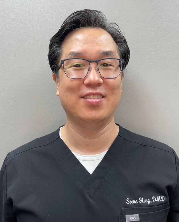 A man wearing glasses and a blue scrub top is smiling for the camera.