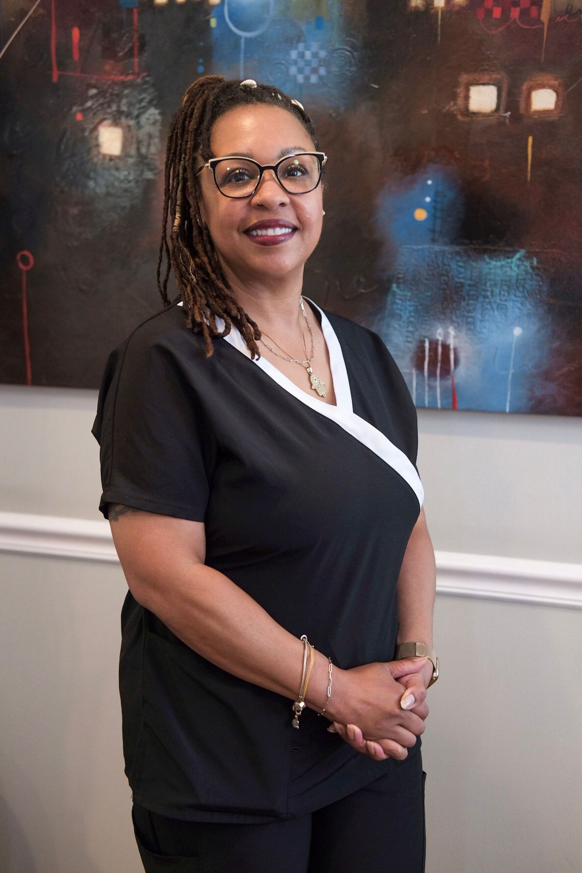 A woman wearing glasses and dreadlocks is smiling for the camera.