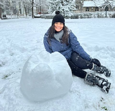 A woman is sitting in the snow next to an igloo.