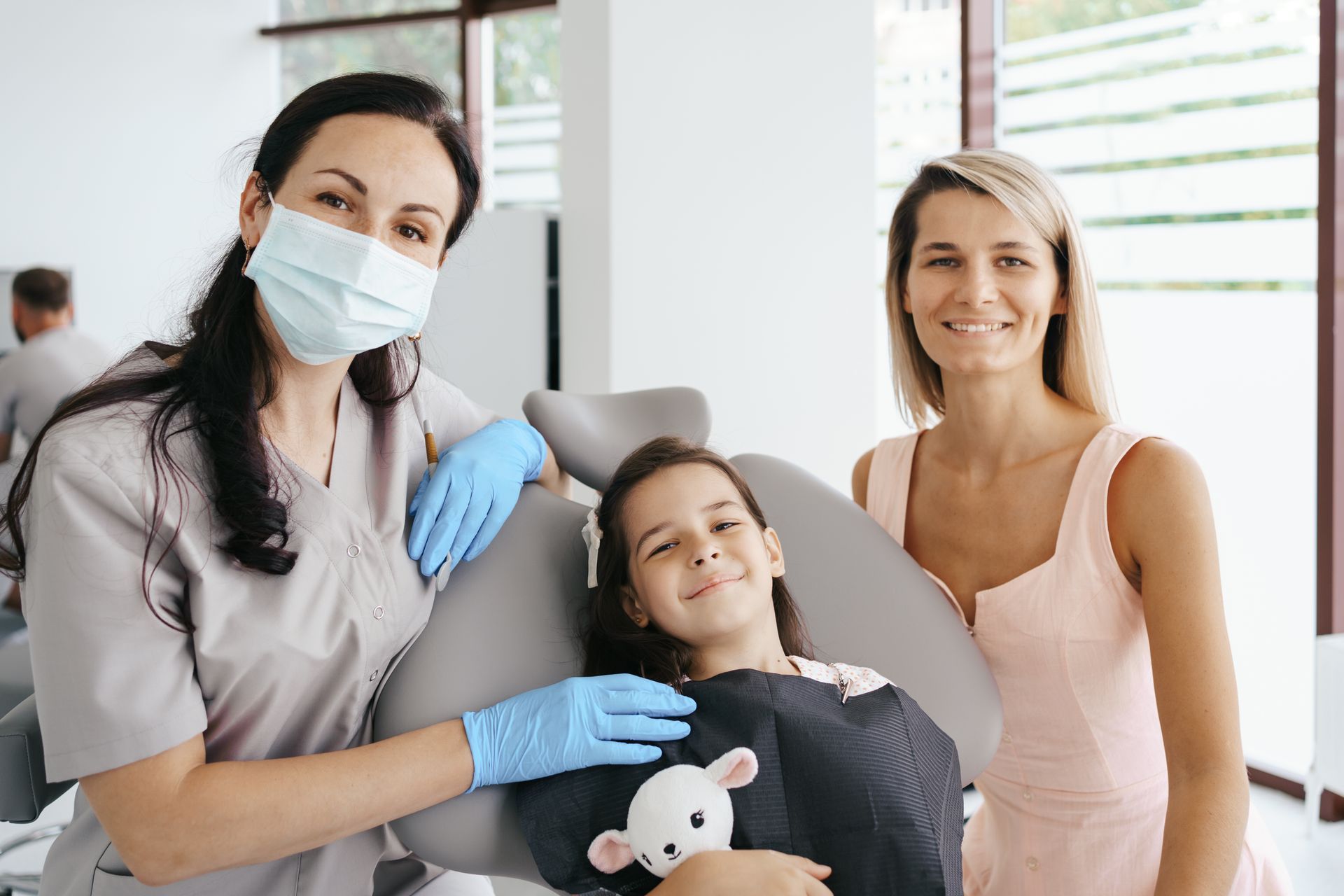 A little girl is sitting in a dental chair with her mother.