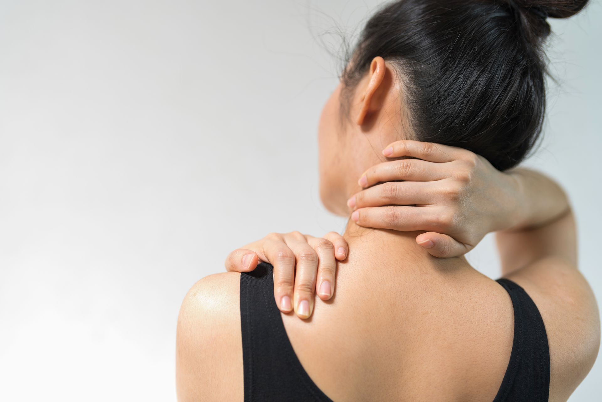 A woman is holding her neck and shoulder in pain.