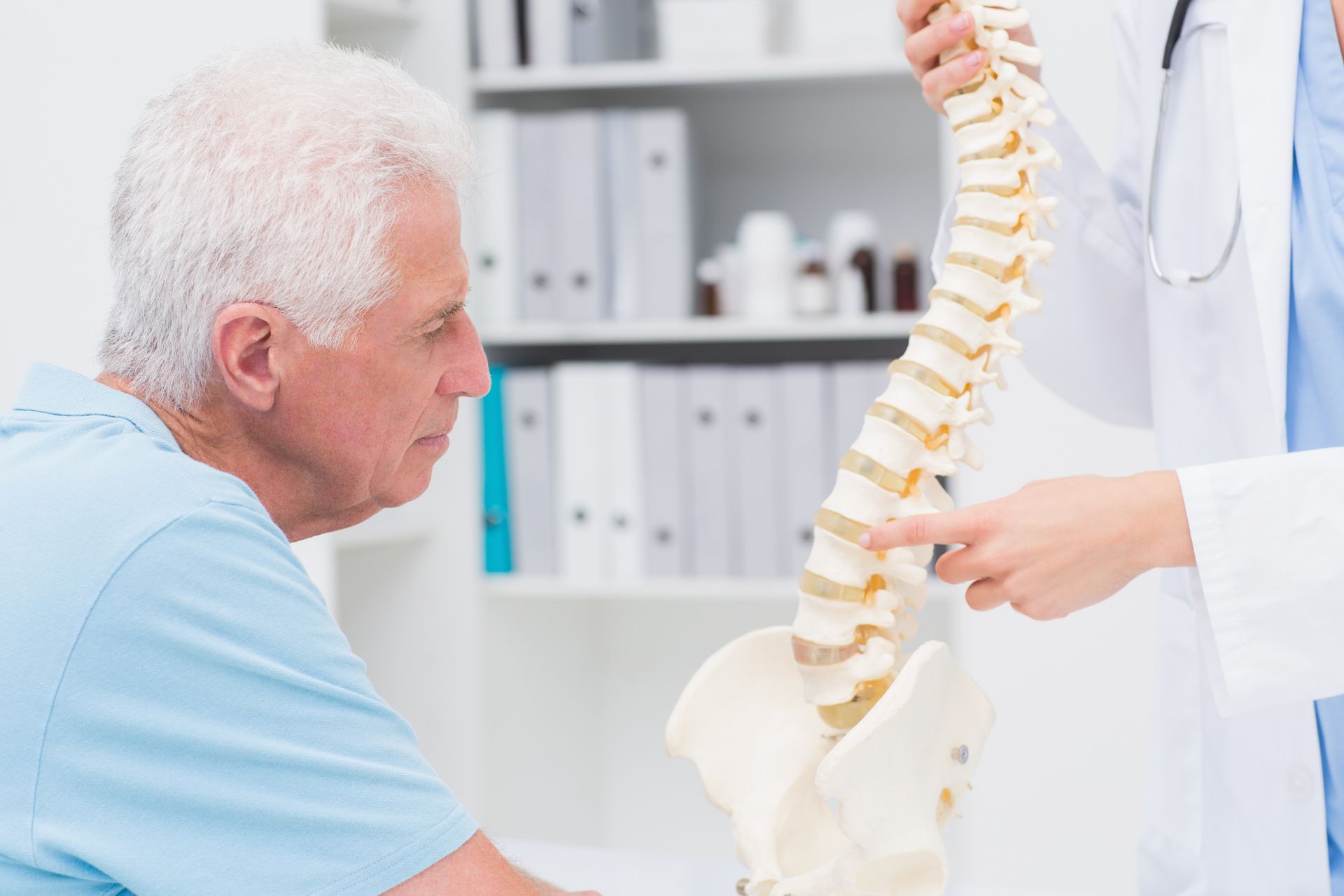 A doctor is showing an elderly man a model of his spine.