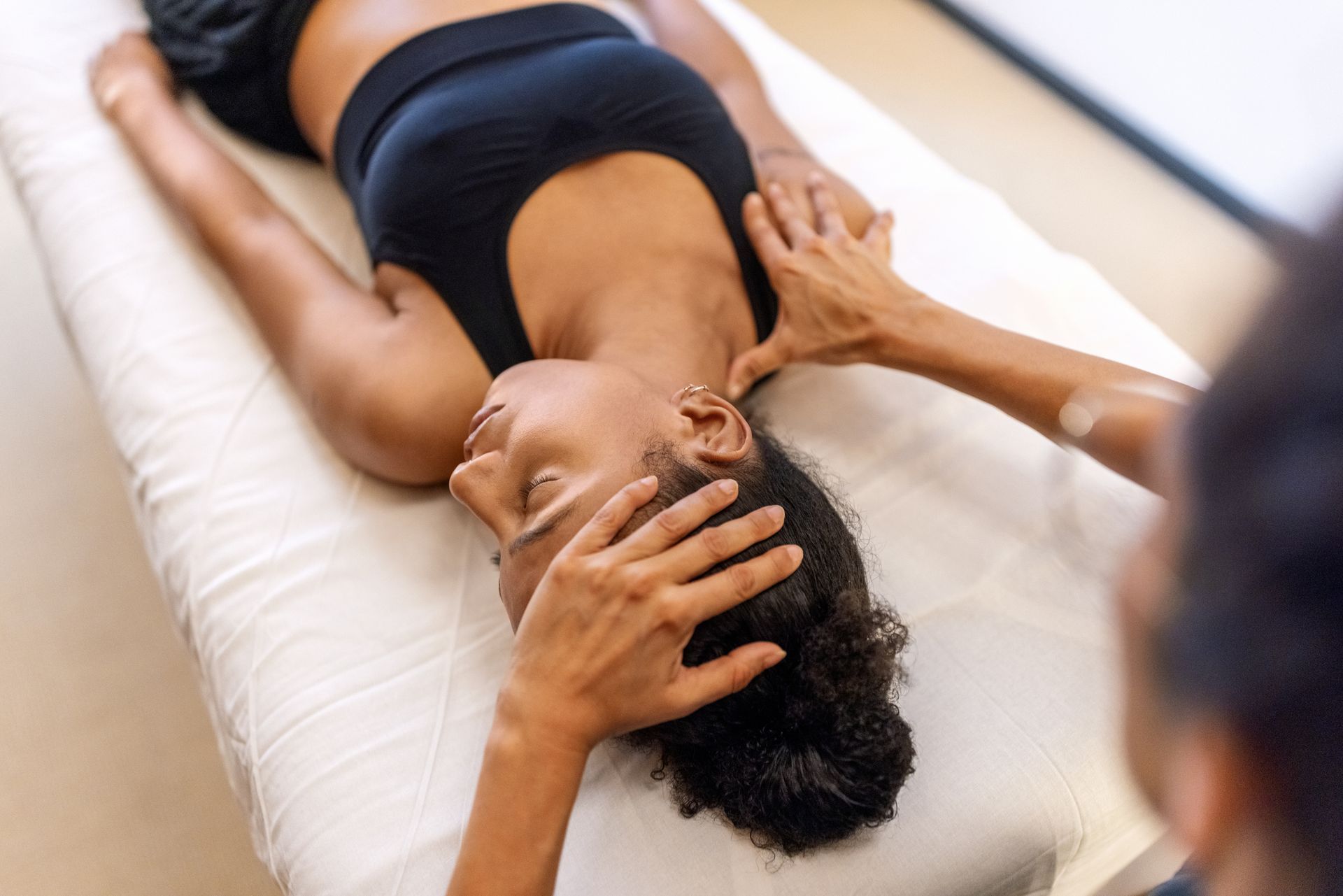 A woman is laying on a bed getting a head massage.