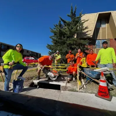 Construction crew in bright safety gear near cut concrete on a sunny day.