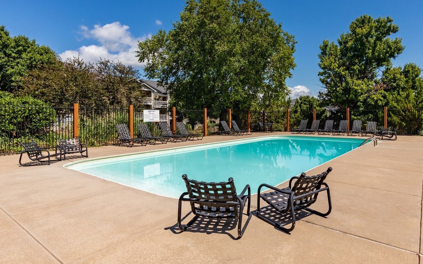 Swimming pool with lounge chairs on concrete patio, surrounded by trees and fence.