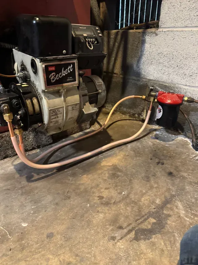 Oil burner system in a basement, Beckett brand. Includes filter, fuel lines and metal components.