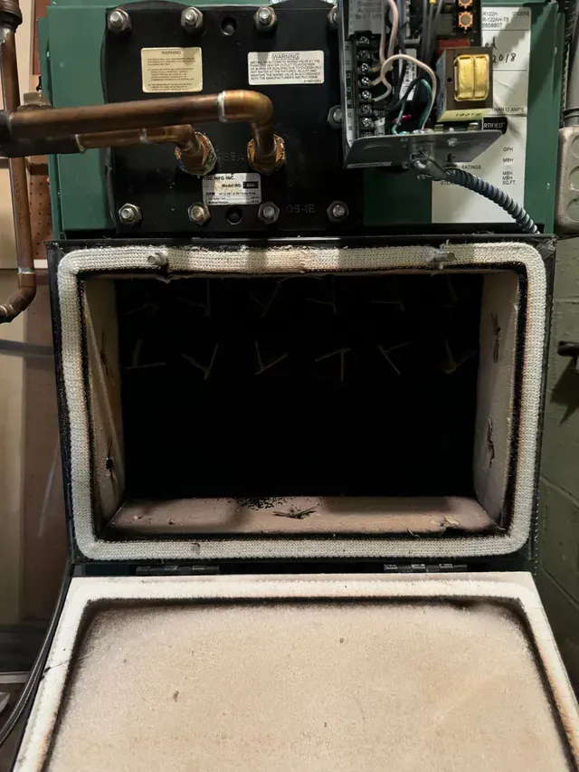 Open furnace chamber with black interior, white insulation, and copper piping.