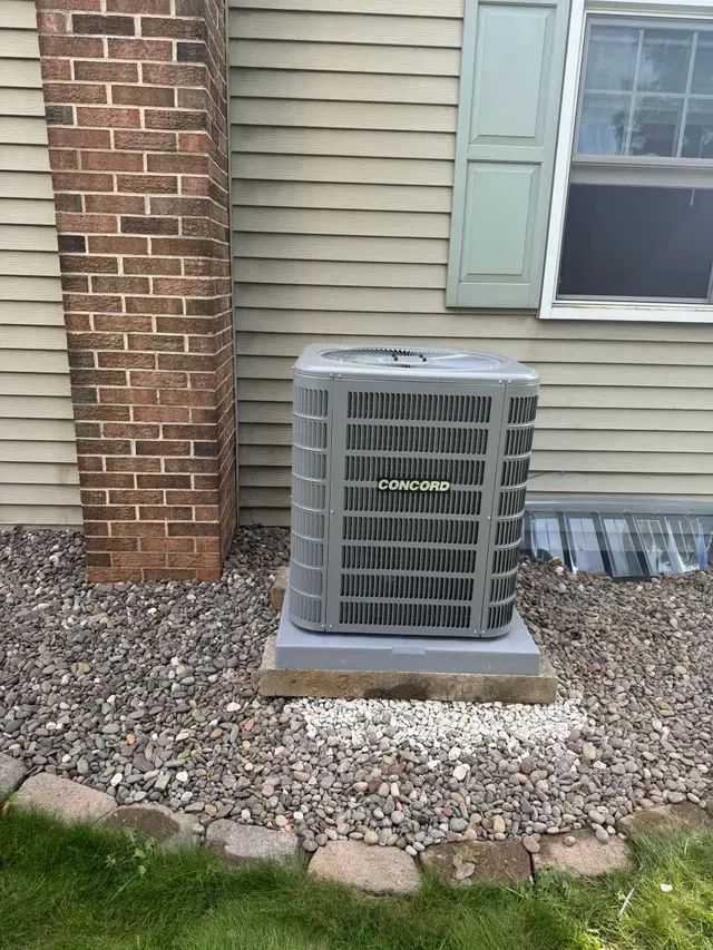 AC unit on a concrete pad next to a brick chimney and a beige house.