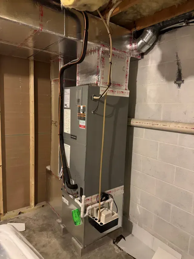 Furnace unit in a basement, ductwork overhead, electrical wiring, white and gray.