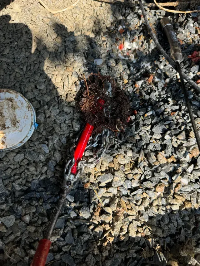 Red rooter tool covered in debris on gravel ground.