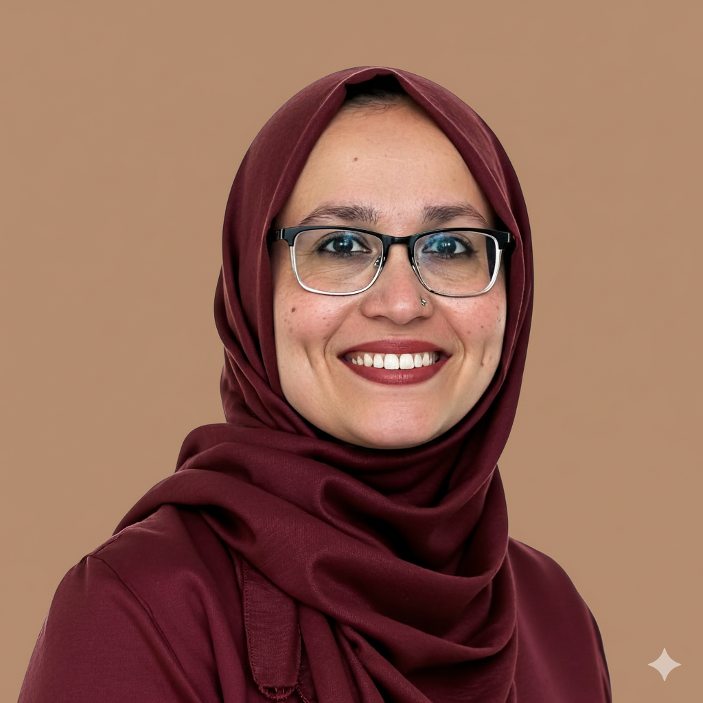 Woman wearing glasses and burgundy hijab smiles at camera.