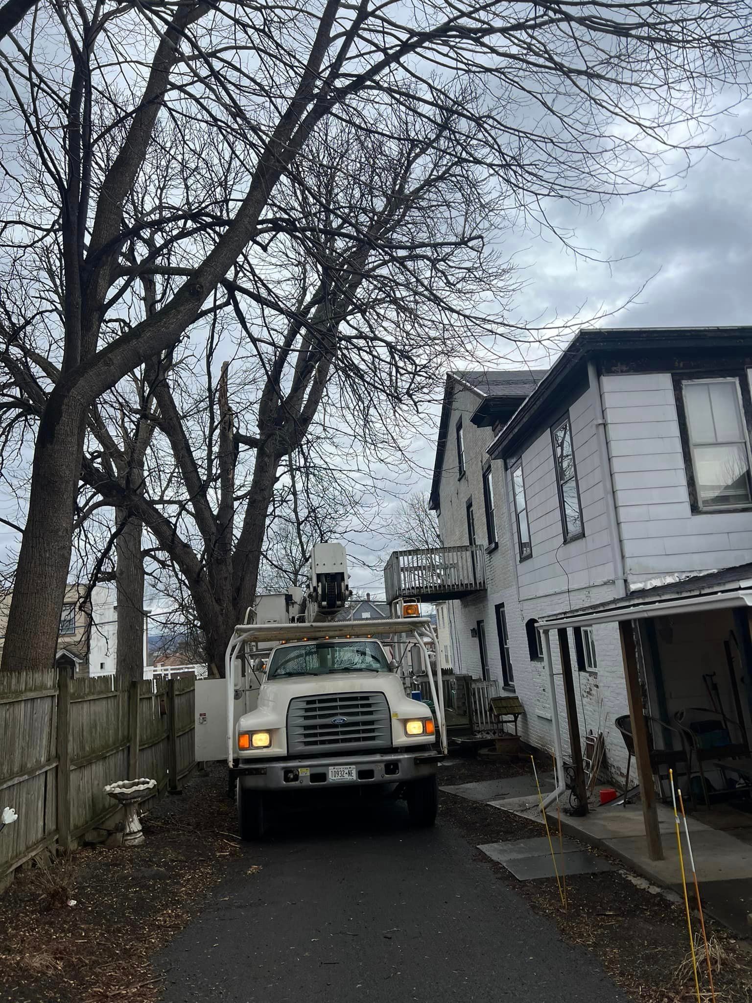 A truck is cutting a tree in front of a house.