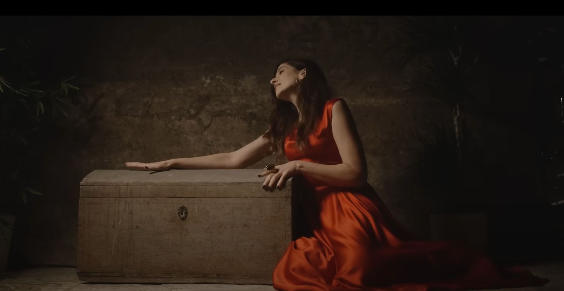 A woman in a red dress is kneeling down next to a trunk.