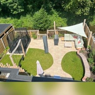 Bovenaanzicht van een achtertuin met een trampoline, tuinmeubilair en kunstgras, omgeven door bomen.