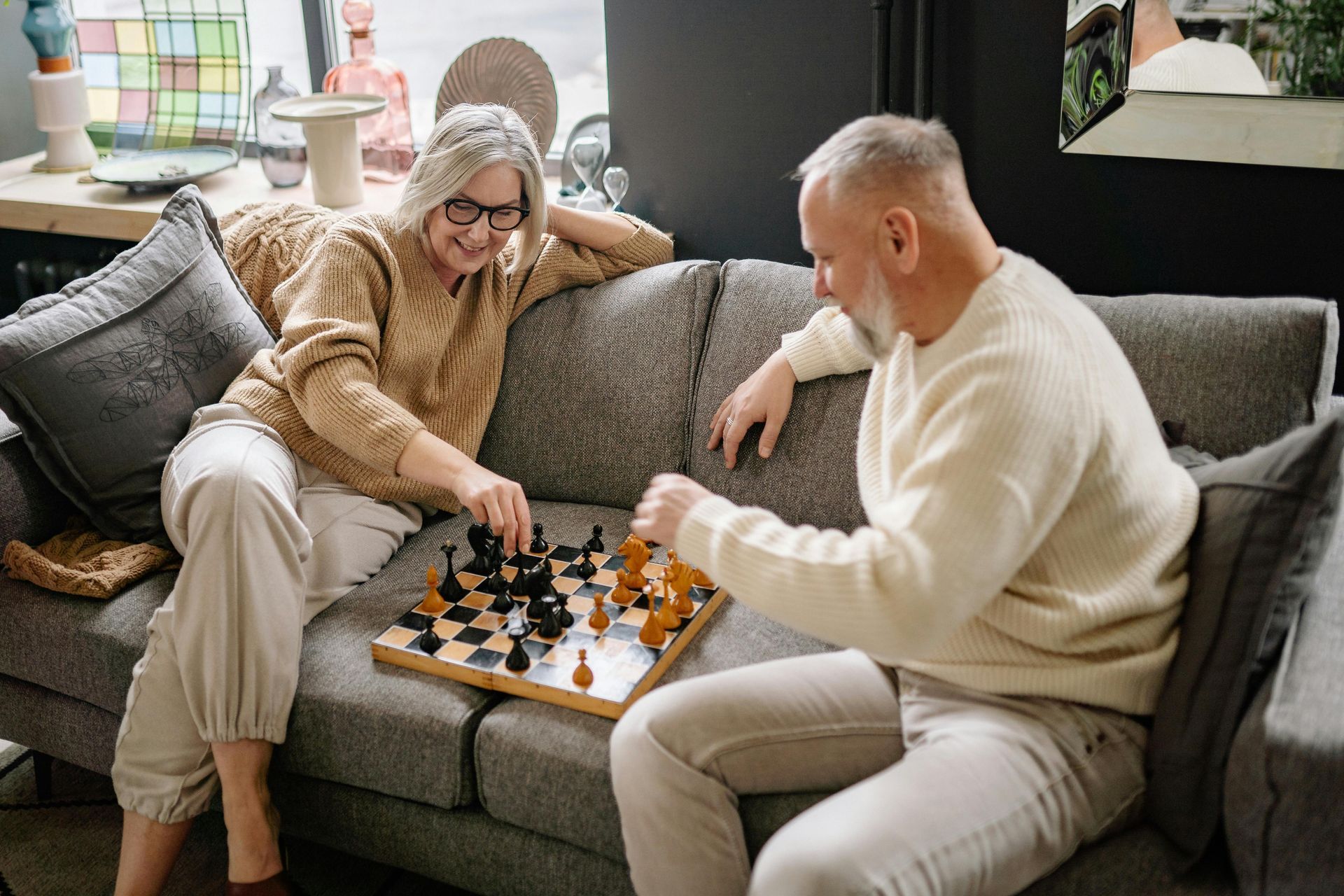 An older couple plays chess on the sofa.