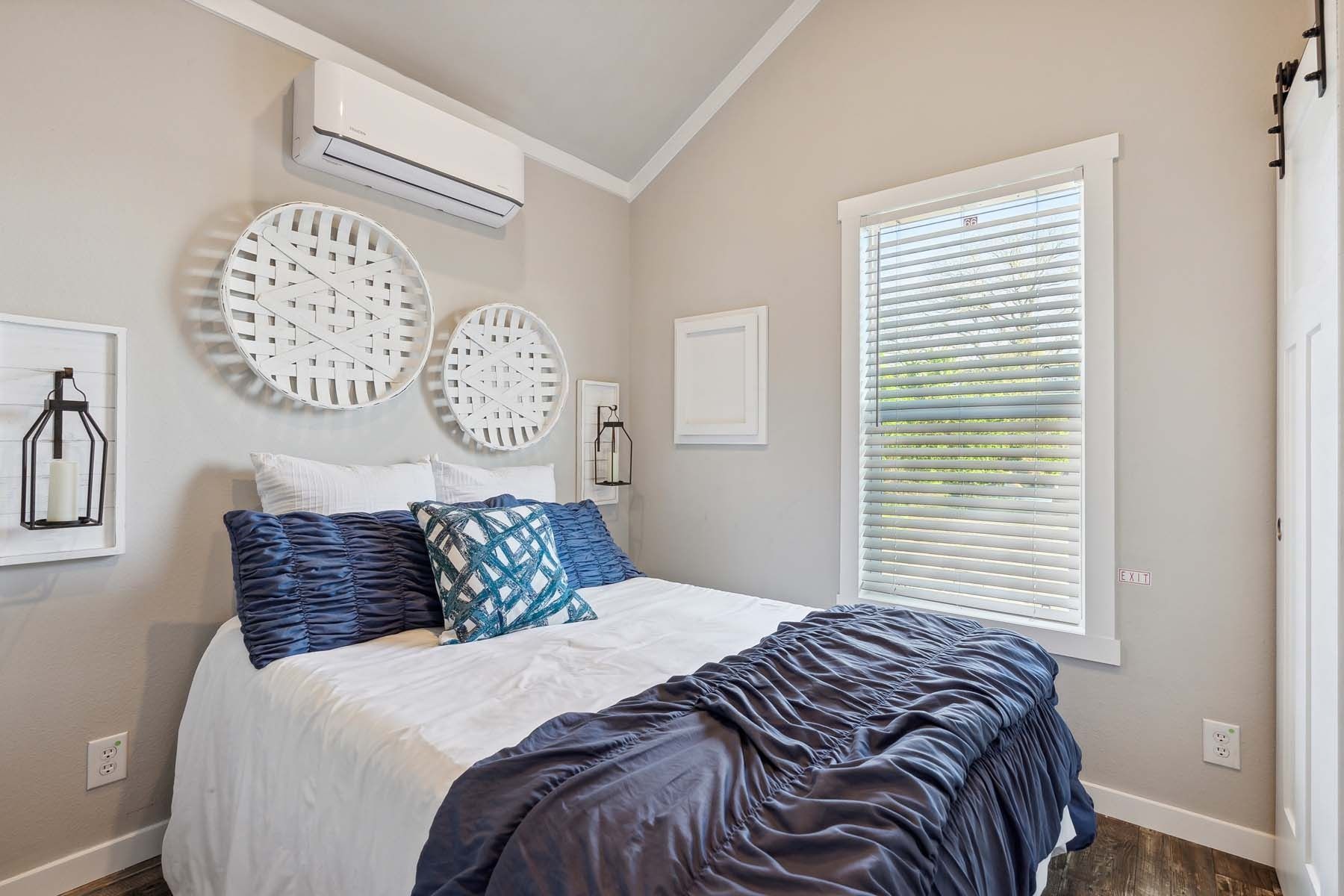 Bright bedroom with a neatly made bed, navy bedding, circular wall decor, and a window with blinds