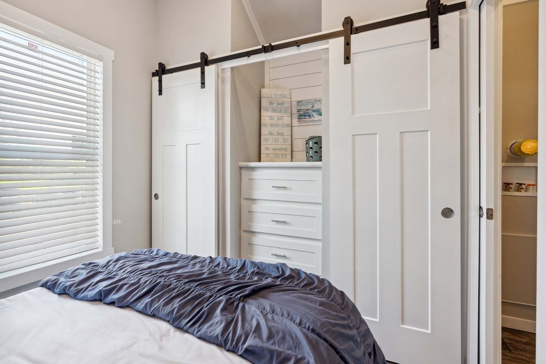 Bedroom with sliding barn doors, white dresser, and a bed with a dark blue comforter near a window