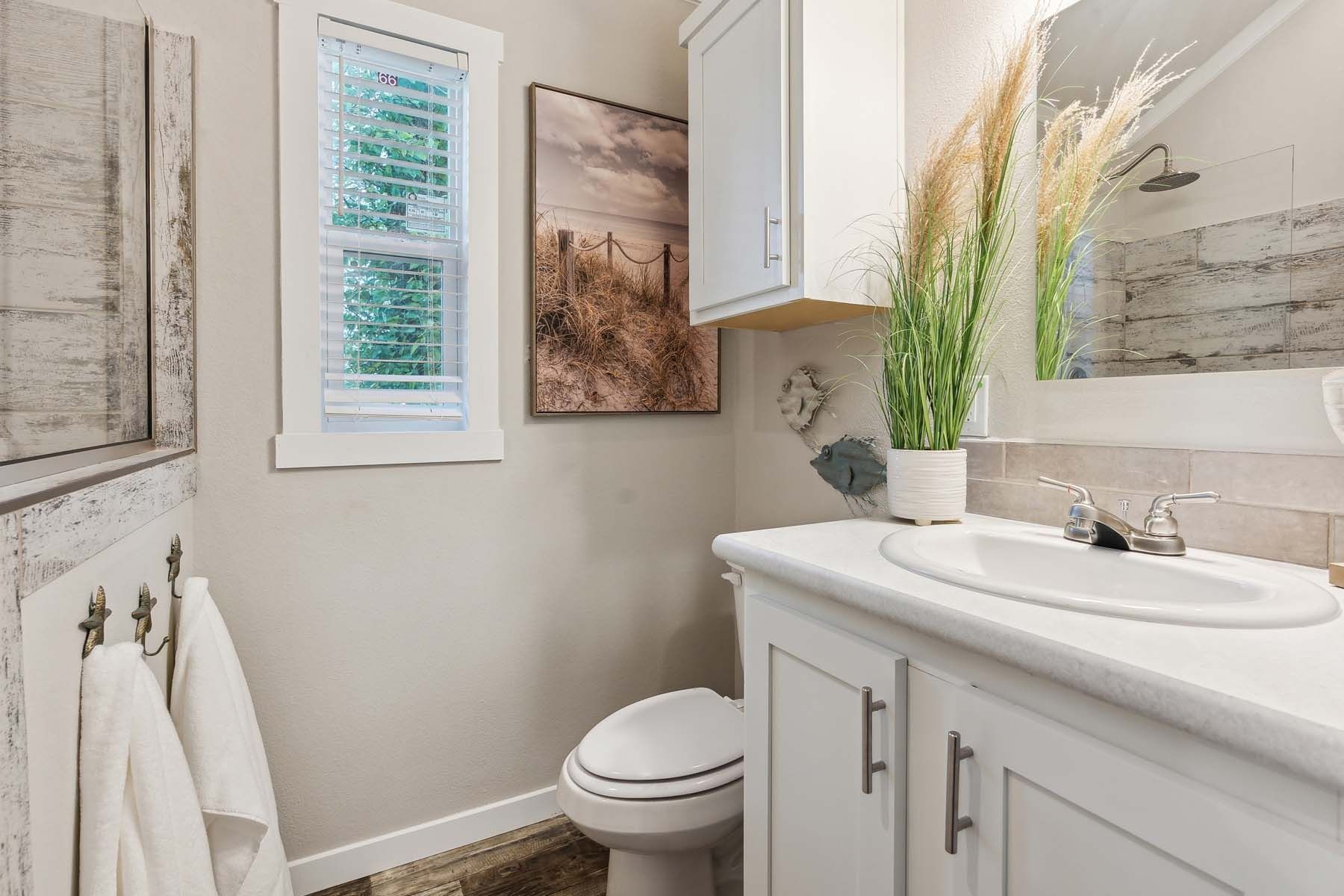Bright modern bathroom with white vanity, toilet, towels, and framed wall art