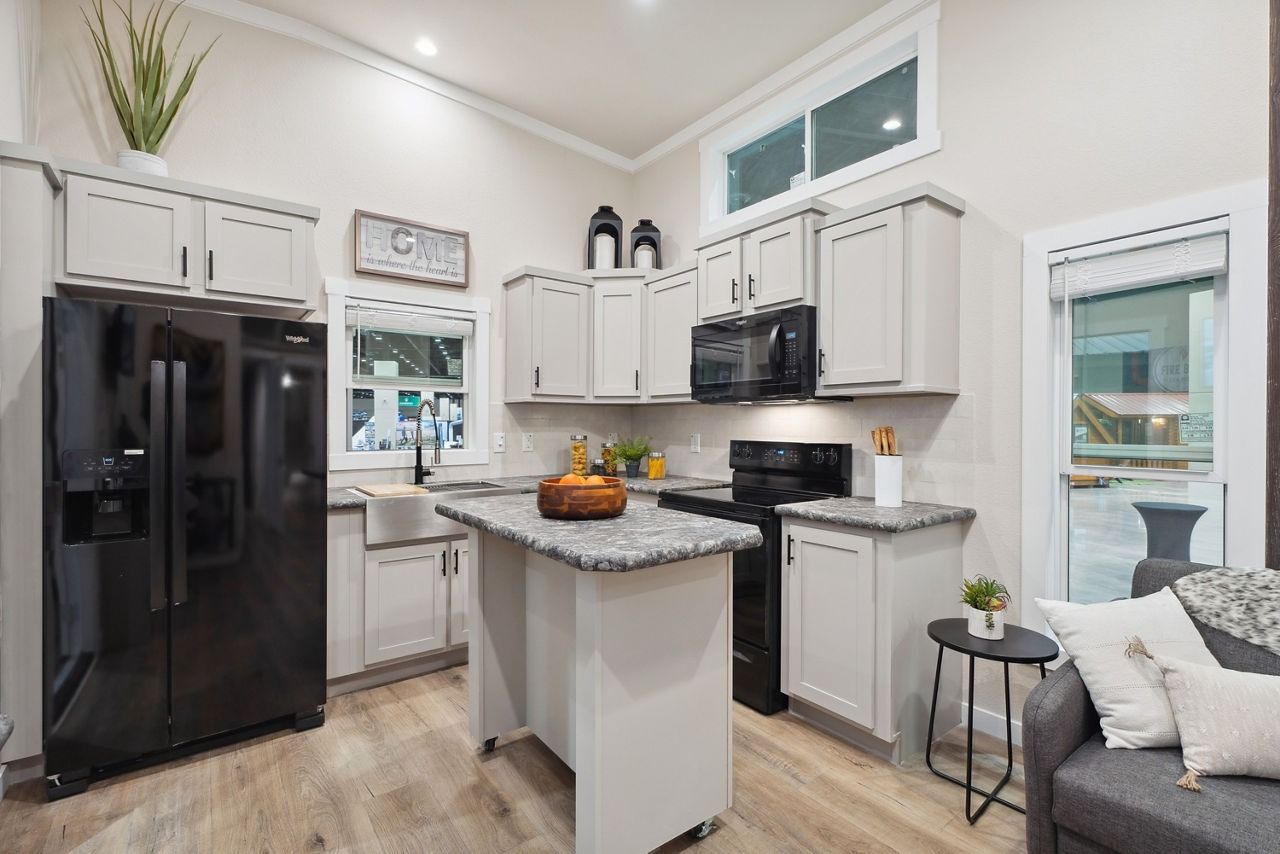 Bright modern kitchen with black appliances, white cabinets, gray island, and adjacent living area