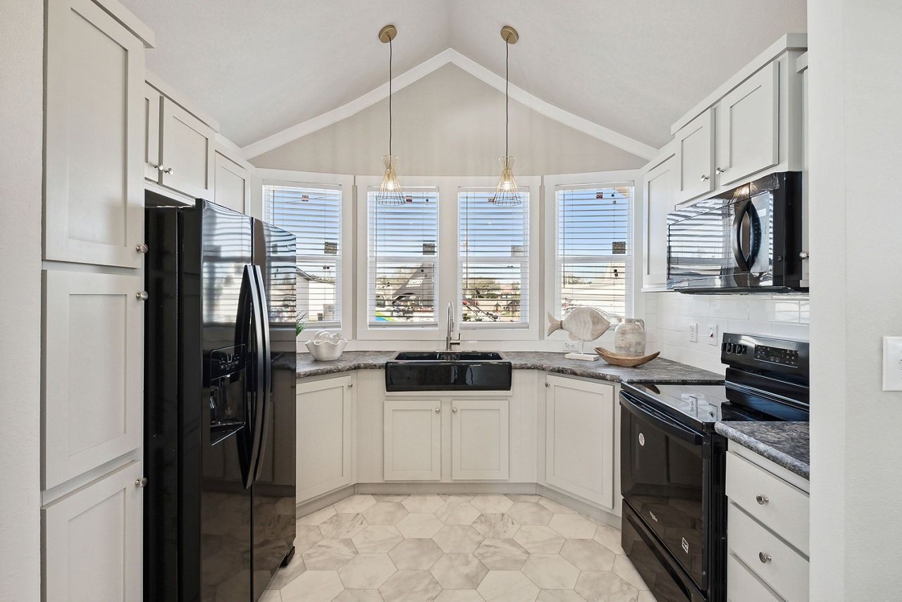 Bright white kitchen with black appliances, marble floor, and large windows overlooking water.