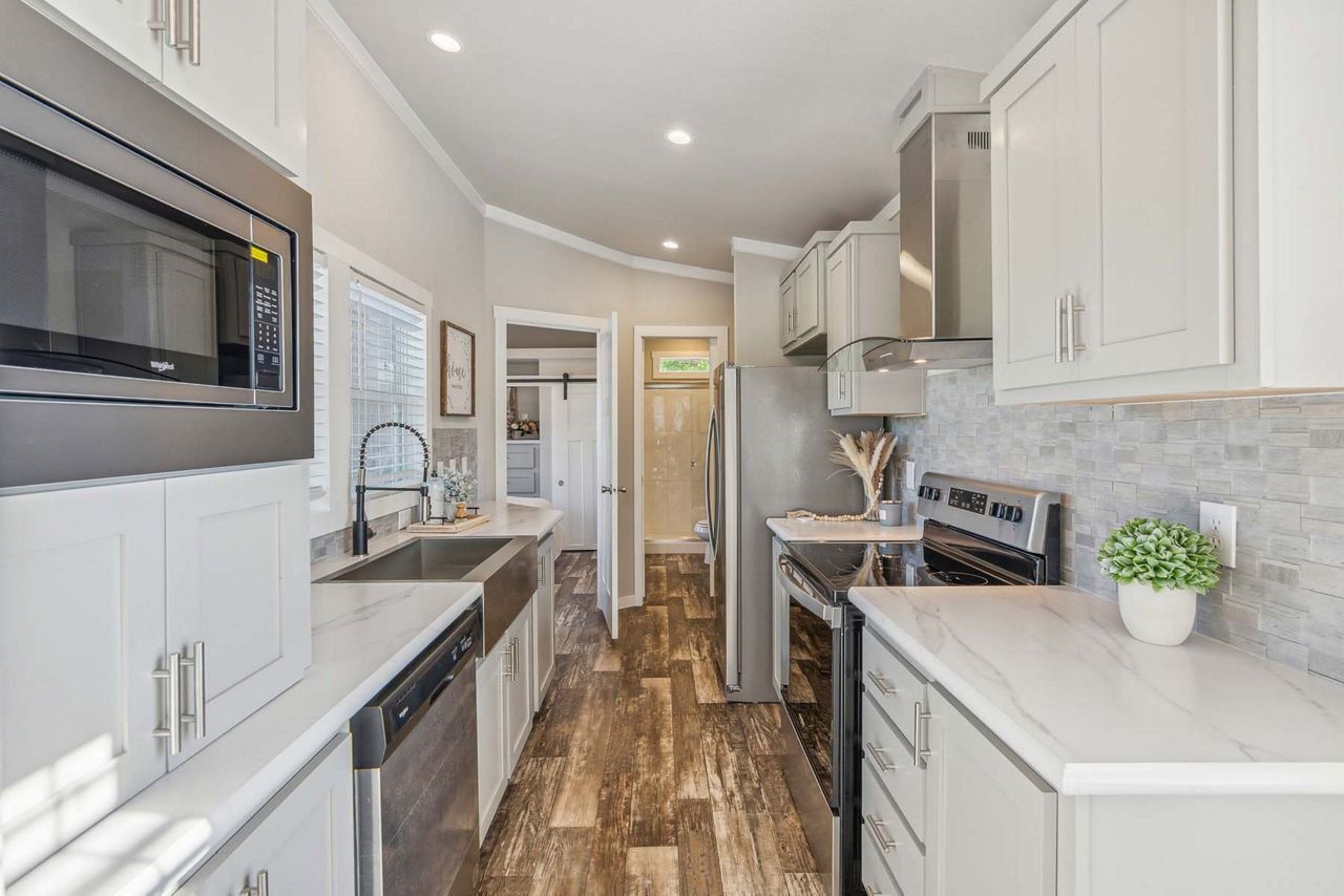 Bright modern galley kitchen with white cabinets, stainless appliances, and wood-look floor