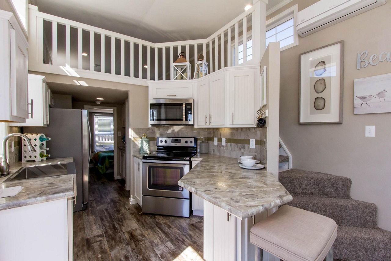 Bright kitchen with white cabinets, stainless steel appliances, granite counters, and a carpeted staircase.