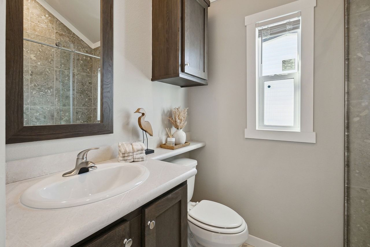 Small modern bathroom with white vanity, dark wood cabinet, mirror, toilet, and frosted window.