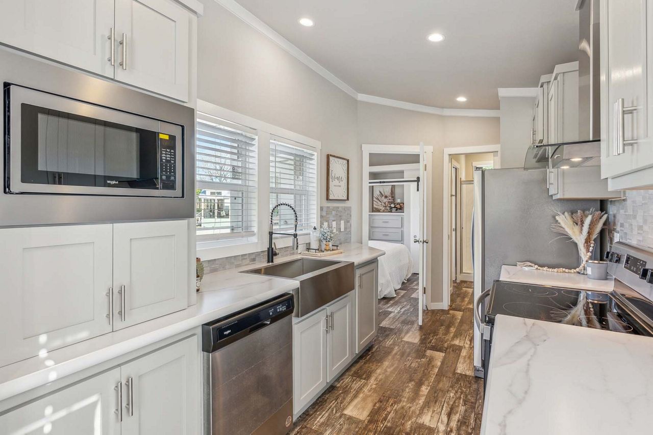Bright modern kitchen with white cabinets, stainless appliances, and wood floors