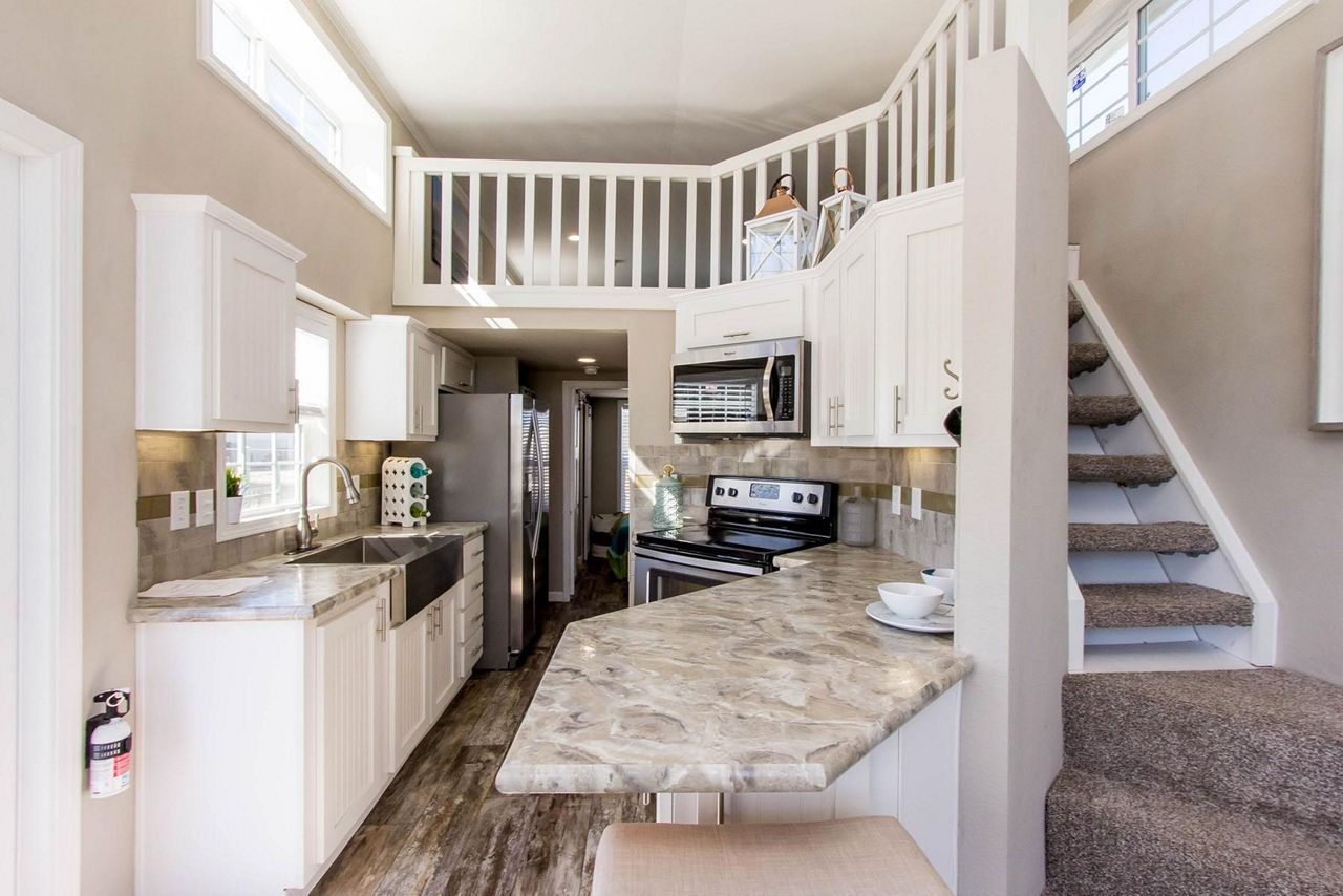 Bright white kitchen with granite counters, stainless appliances, and carpeted stairs leading to a loft.