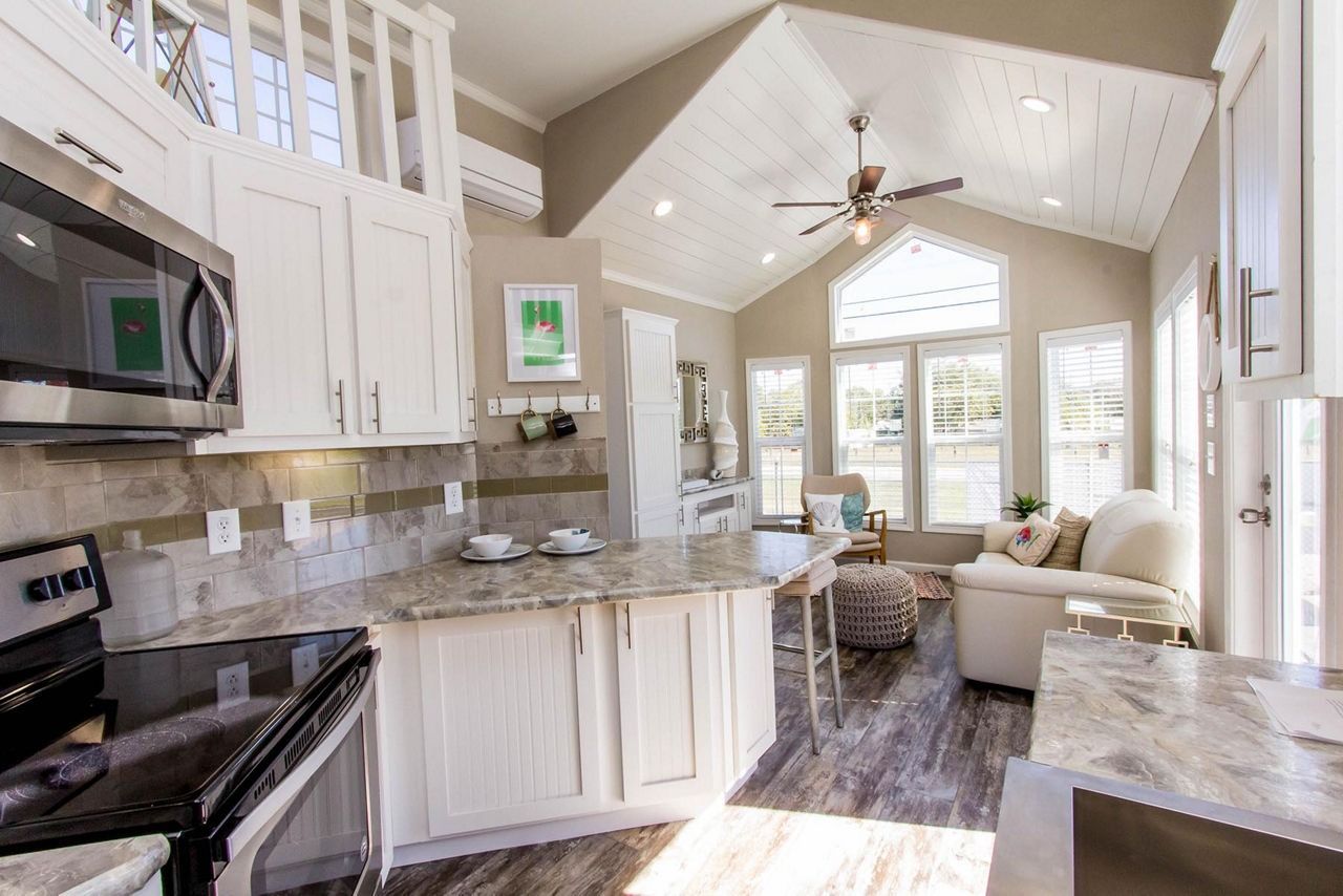 Bright white kitchen with granite counters, stainless appliances, and a vaulted ceiling opening to a sunlit living area
