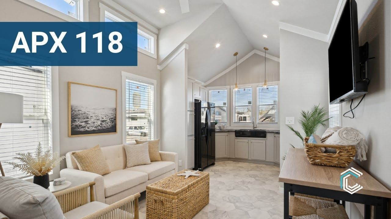 Bright living room with beige sofa, wicker chairs, wall art, and large windows under a vaulted ceiling.