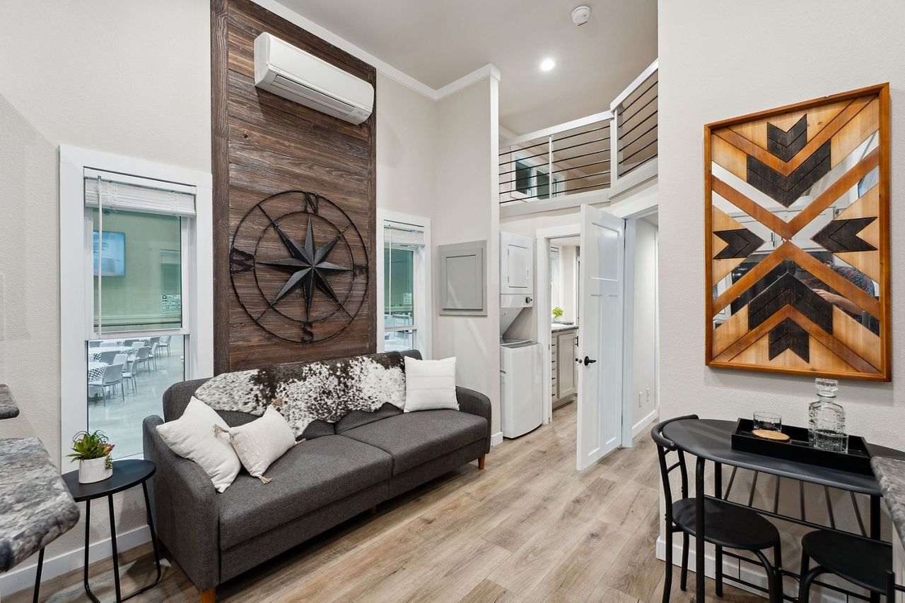 Modern living room with gray sofa, tall wall decor, wood floors, and geometric artwork in a bright loft space