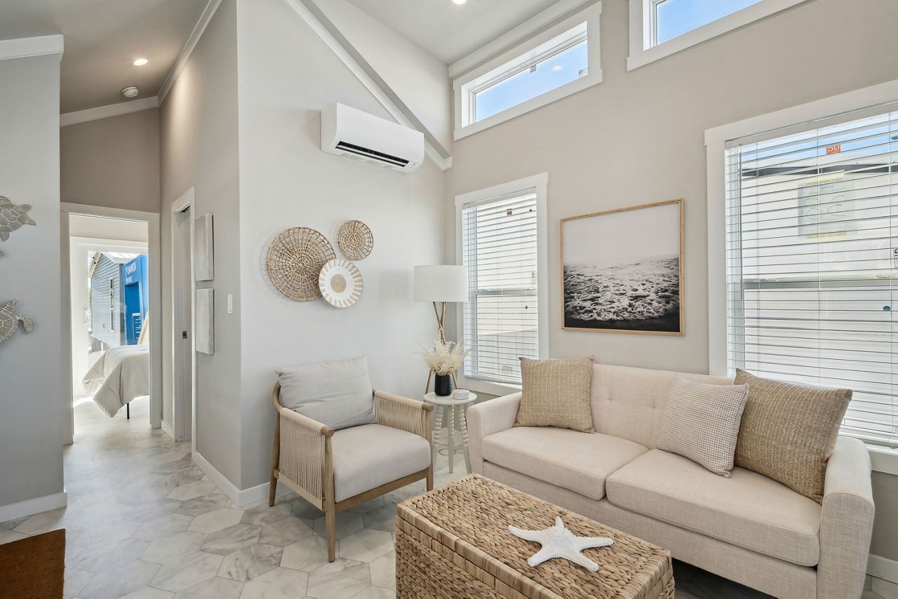 Bright living room with beige sofa, wicker chair, wall art, and tall windows with blinds