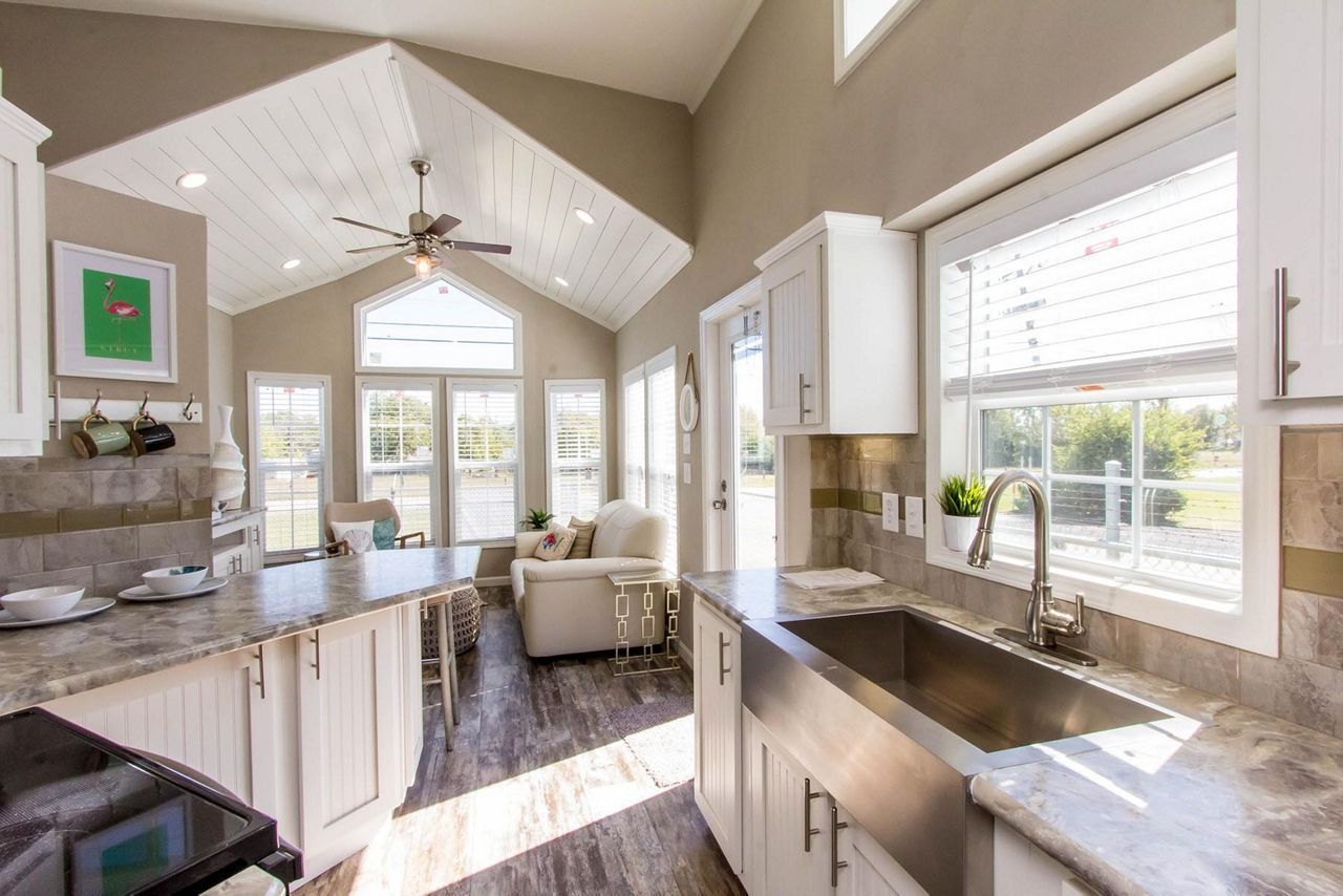 Bright modern kitchen with white cabinets, large windows, island, and vaulted ceiling