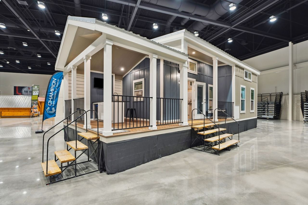 Tiny modern house on display at an indoor expo, with beige siding, white trim, and front porch steps
