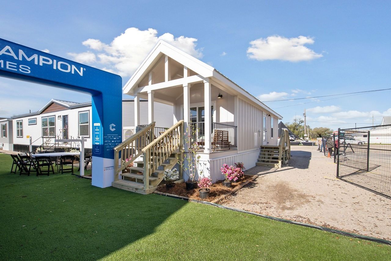 White tiny house model with porch and stairs at a real estate display booth outdoors