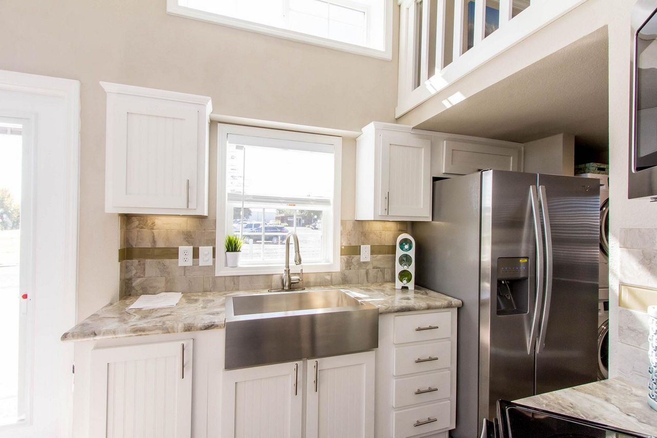 Bright kitchen with white cabinets, granite countertops, stainless steel sink, and refrigerator under high windows.