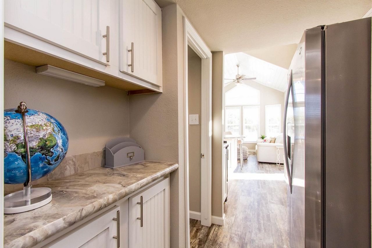 Bright kitchen pass-through with white cabinets, marble countertop, and a view into a sunlit living area.